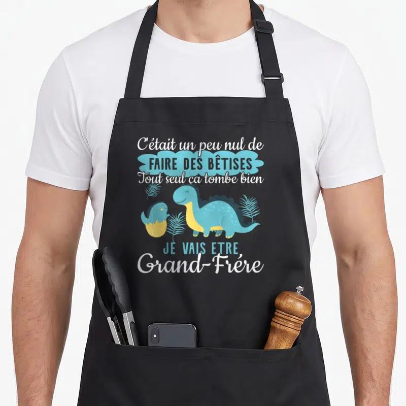 Tablier de cuisine noir avec un dinosaure bleu, un œuf jauni et le texte Je vais être Grand-Frère imprimé en blanc et bleu.