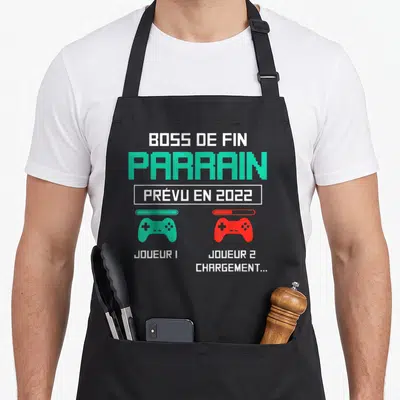 Tablier de cuisine noir avec texte Boss de fin Parrain et deux manettes de jeu vertes et rouges.