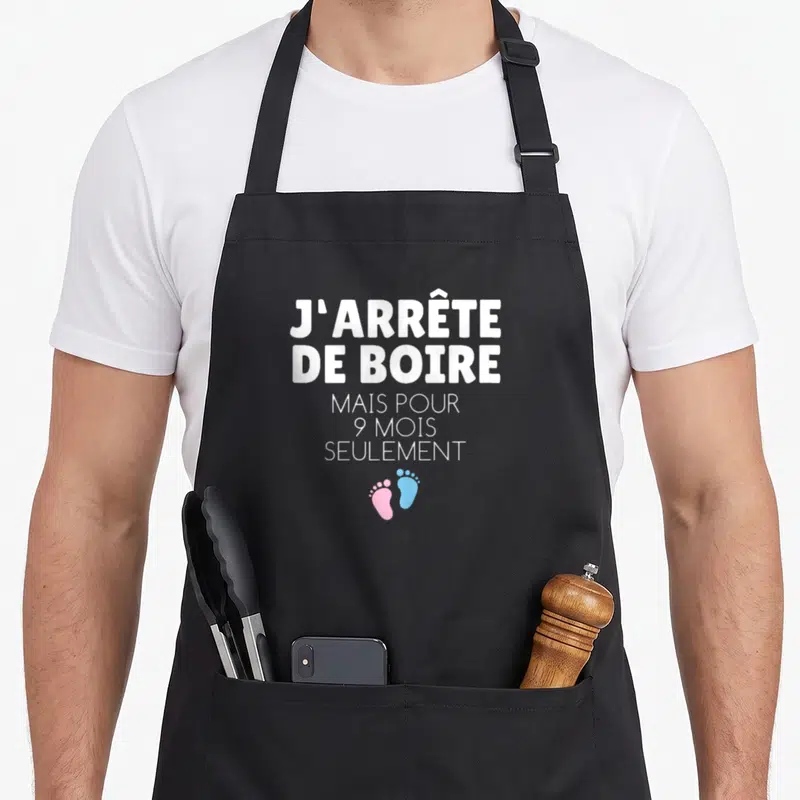 Tablier de cuisine noir avec texte blanc J'arrête de boire mais pour 9 mois seulement et deux petits pieds rose et bleu.