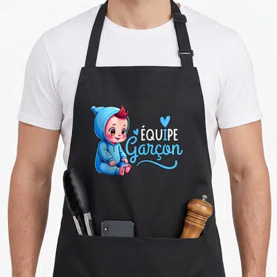 Tablier de cuisine noir avec illustration d'un bébé en pyjama bleu et le texte Équipe Garçon en typographie stylisée.