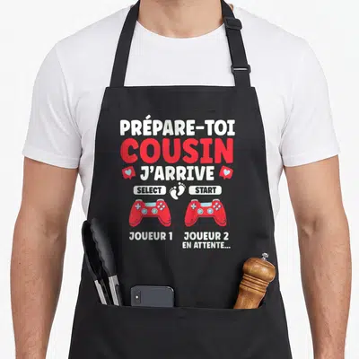Tablier de cuisine noir avec texte Prépare-toi Cousin J'arrive, deux manettes rouges et une empreinte de pied blanche entre les boutons Select et Start.