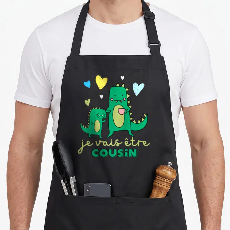 Tablier de cuisine noir avec deux dinosaures verts et le texte je vais être cousin entouré de cœurs colorés.