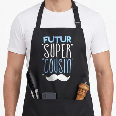 Tablier de cuisine noir avec l'inscription Futur Super Cousin en bleu et blanc, orné d'étoiles et d'une moustache stylisée.