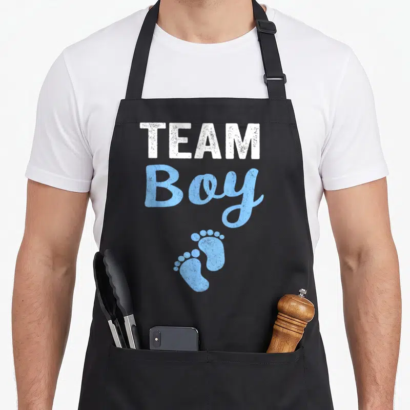 Tablier de cuisine noir avec l'inscription Team Boy et deux petites empreintes de pieds bleues en dessous du texte.