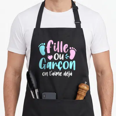 Tablier de cuisine noir avec l'inscription Fille ou Garçon on t'aime déjà en rose et bleu, orné de petits pieds.