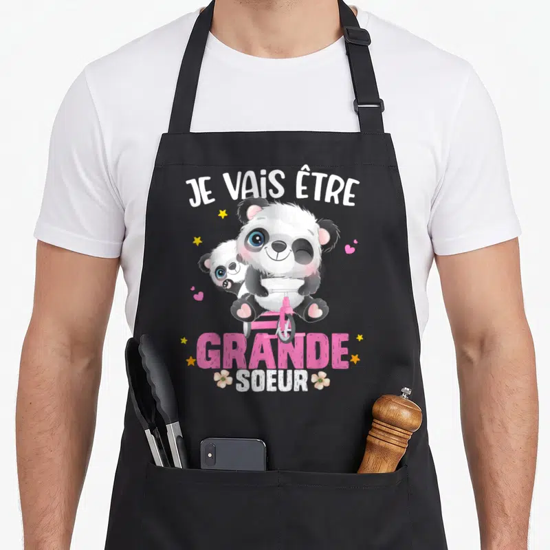 Tablier de cuisine noir avec illustration panda sur tricycle rose et texte Je vais être grande soeur entouré d'étoiles et de fleurs.