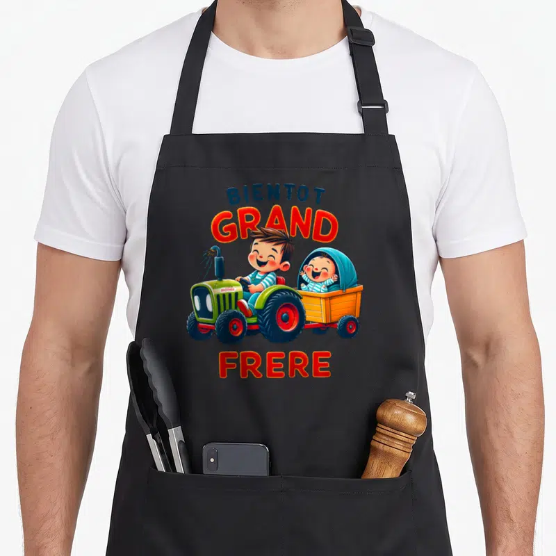 Tablier de cuisine noir avec un garçon au volant d'un tracteur vert tirant une remorque avec un bébé souriant.