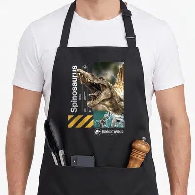Tablier de cuisine noir avec illustration réaliste d'un Spinosaure émergeant de l'eau et texte blanc vertical.