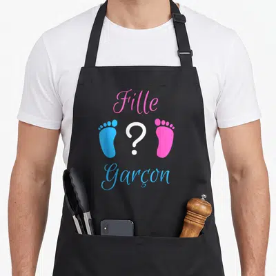Tablier de cuisine noir avec l'inscription Fille et Garçon entourée d'empreintes de pieds colorées et d'un point d'interrogation central.