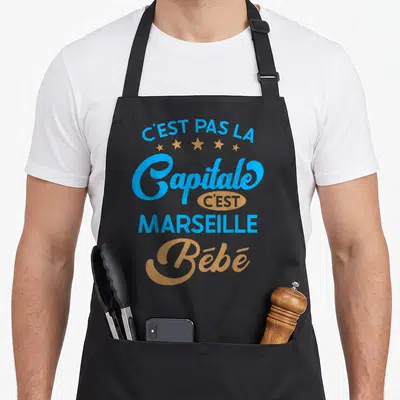 Tablier de cuisine noir avec inscription C'est pas la capitale c'est Marseille Bébé en bleu et or.