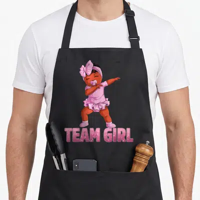 Tablier de cuisine noir avec une babygirl noire en tenue rose effectuant un dab sous le texte Team Girl.