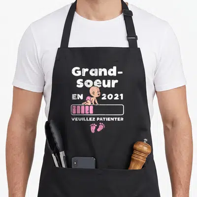 Tablier de cuisine noir avec l'illustration d'un bébé et le texte Grande Soeur en 2021 Veuillez patienter.