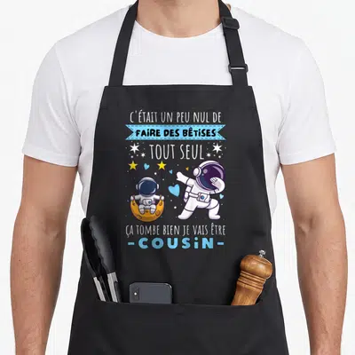 Tablier de cuisine noir avec deux astronautes et le texte Je vais être cousin en bleu et blanc.