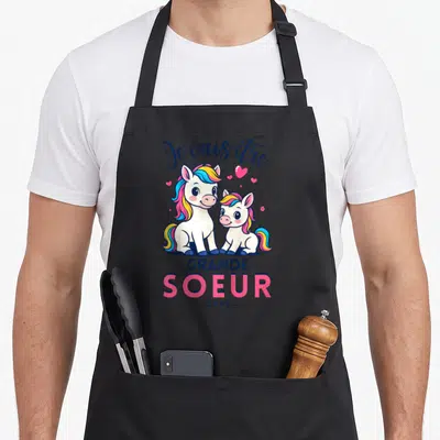 Tablier de cuisine noir avec deux licornes colorées et le texte Je vais être Grande Soeur 2026 en typographie stylisée.
