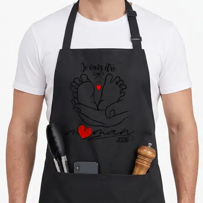 Tablier de cuisine noir avec illustration de mains tenant des pieds de bébé et texte Je vais être maman 2026.