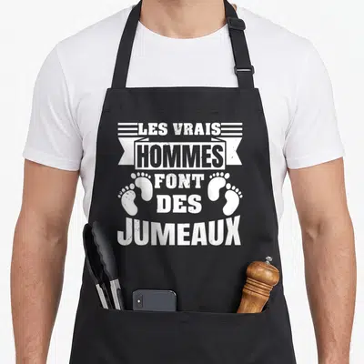 Tablier de cuisine noir avec inscription blanche Les vrais hommes font des jumeaux et deux empreintes de pieds de bébé.