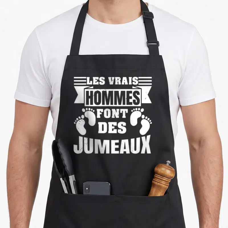 Tablier de cuisine noir avec inscription blanche Les vrais hommes font des jumeaux et deux empreintes de pieds de bébé.