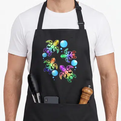 Tablier de cuisine noir avec quatre bébés tortues de mer multicolores et des bulles aquatiques.