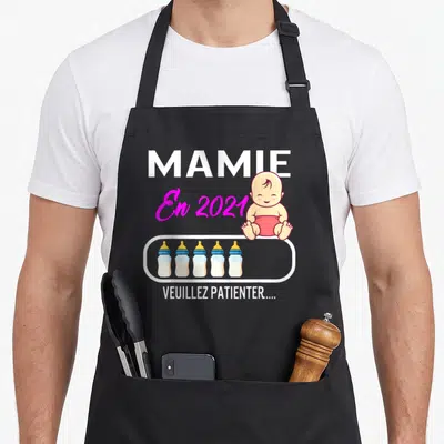 Tablier de cuisine noir avec illustration d'un bébé, cinq biberons et le texte Mamie En 2021 Veuillez patienter.