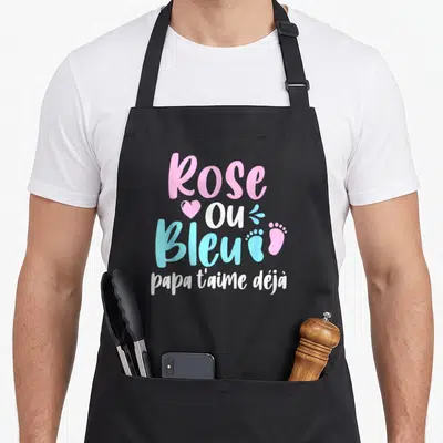 Tablier de cuisine noir avec l'inscription Rose ou Bleu papa t'aime déjà en rose et bleu, orné d'un cœur et de petits pieds.