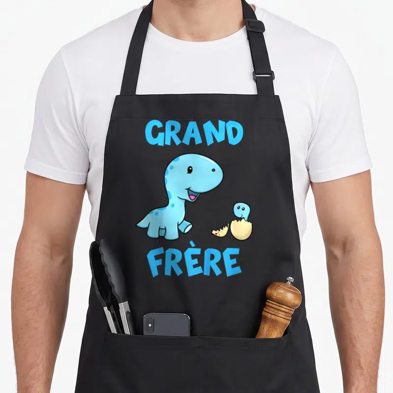 Tablier de cuisine noir avec un dinosaure bleu souriant et un œuf éclos portant l'inscription Grand Frère en lettres capitales.