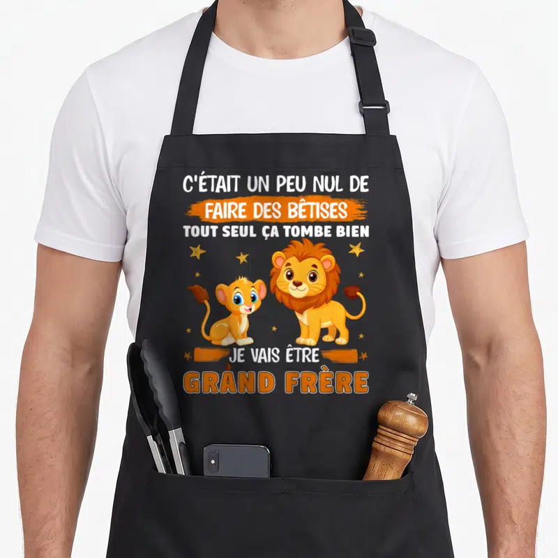 Tablier de cuisine noir avec Simba, Scar et le texte Je vais être grand frère imprimé en orange et blanc.
