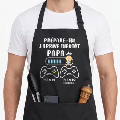 Tablier de cuisine noir avec texte blanc Prépare-toi j'arrive bientôt Papa et illustration de manettes de jeu vidéo avec bébé.
