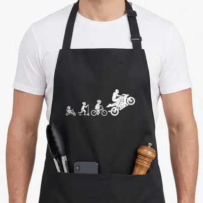 Tablier de cuisine noir avec silhouette blanche montrant un enfant passant du tricycle à la moto sport.