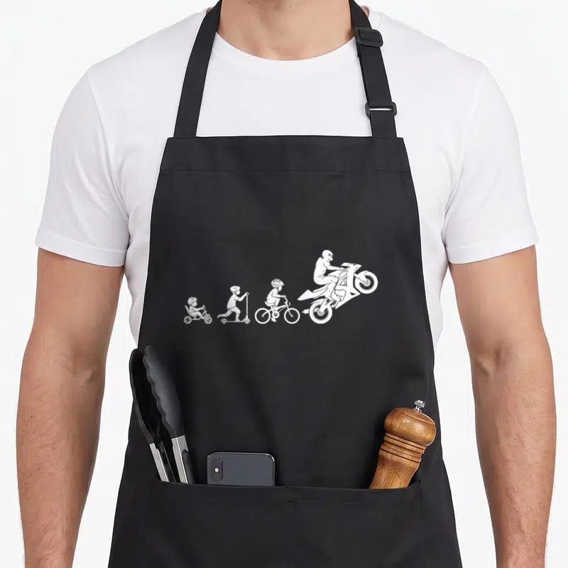 Tablier de cuisine noir avec silhouette blanche montrant un enfant passant du tricycle à la moto sport.