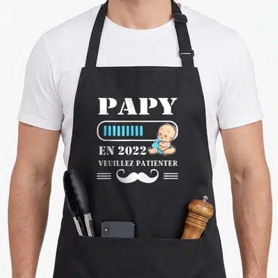 Tablier de cuisine noir avec l'inscription Papy en 2022 Veuillez patienter et un dessin de bébé.