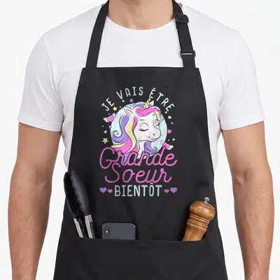 Tablier de cuisine noir avec une licorne colorée et l'annonce Je vais être grande sœur bientôt.