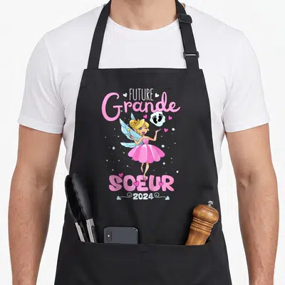 Tablier de cuisine noir avec une fée rose et le texte Future Grande Soeur 2024 imprimé au centre.