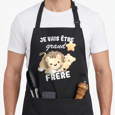 Tablier de cuisine noir avec inscription Je vais être grand frère 2026 et deux lions en dessin animé tenant une étoile.