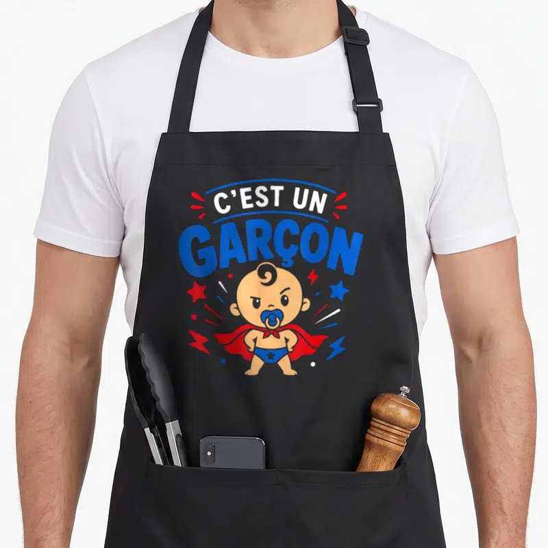 Tablier de cuisine noir avec illustration d'un bébé super-héros et le texte C'est un garçon en lettres bleues et blanches.