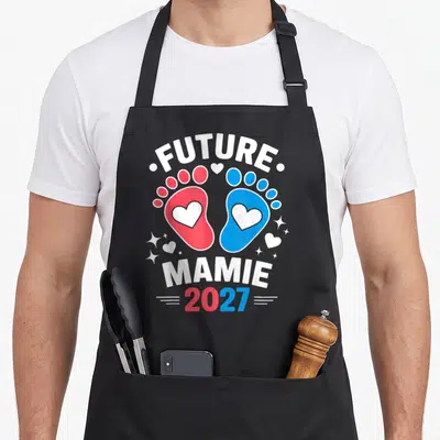 Tablier de cuisine noir avec Future Mamie 2027 et empreintes de pieds rouge et bleue ornées de cœurs blancs.