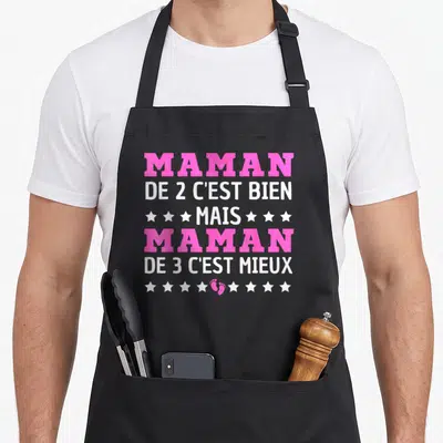 Tablier de cuisine noir avec texte rose et blanc annonçant maman de trois enfants entouré d'étoiles et d'une empreinte de pied.