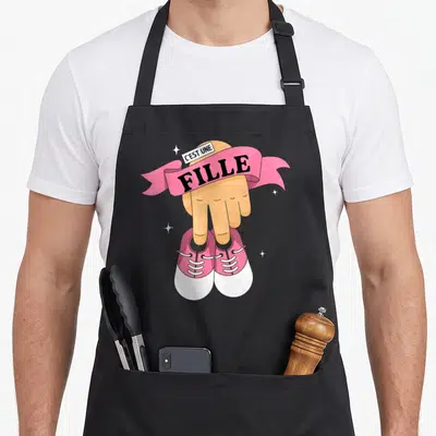 Tablier de cuisine noir avec une main pointant vers des chaussettes roses et le texte C'est une Fille.