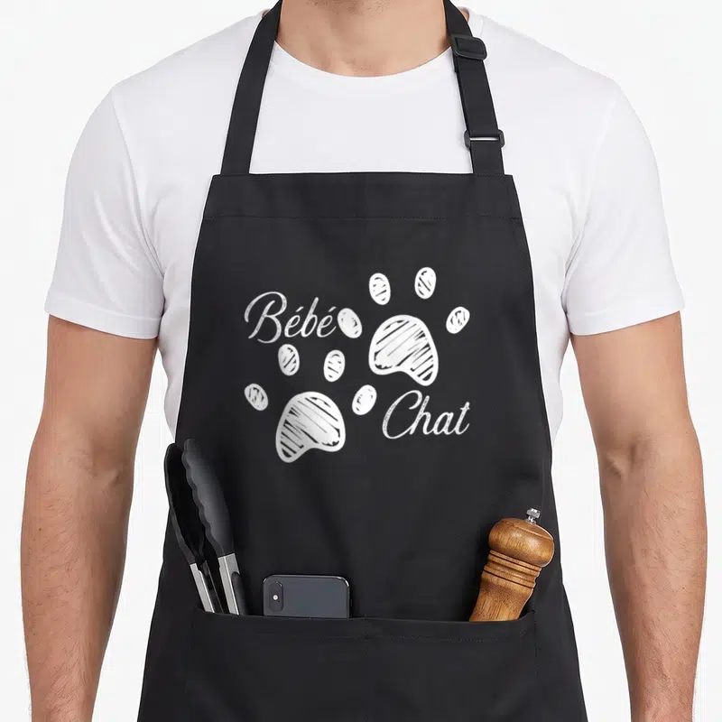 Tablier de cuisine noir avec inscription Bébé Chat et deux traces de pattes blanches stylisées au centre.