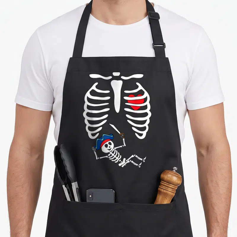 Tablier de cuisine noir avec illustration squelette pirate et cage thoracique contenant un cœur rouge.