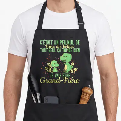 Tablier de cuisine noir avec deux dinosaures verts et le texte annonce grossesse grand frère en vert et jaune.