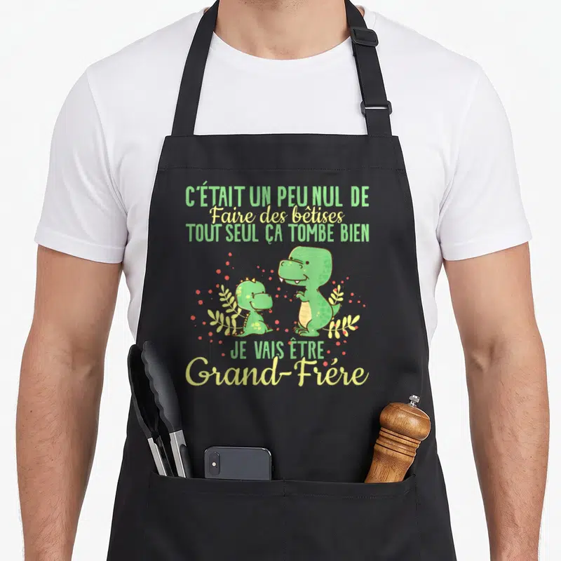 Tablier de cuisine noir avec deux dinosaures verts et le texte annonce grossesse grand frère en vert et jaune.