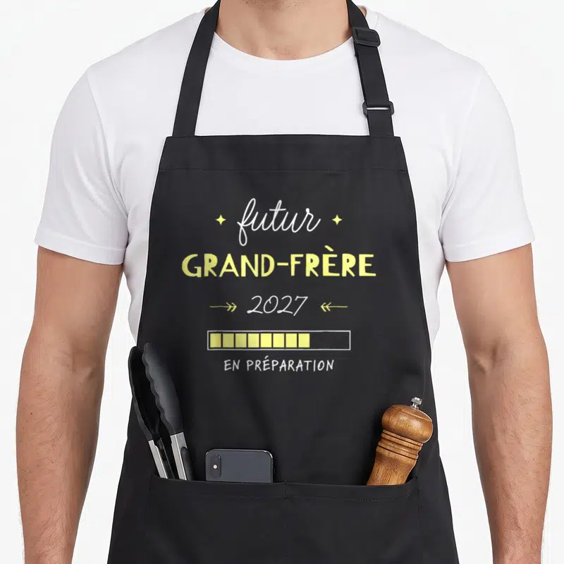 Tablier de cuisine noir avec texte futur grand-frère 2027 et barre de chargement jaune en préparation.