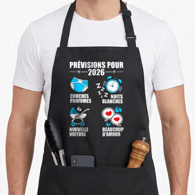 Tablier de cuisine noir avec illustrations de couches, réveil et poussette sur le thème des prévisions pour 2026.