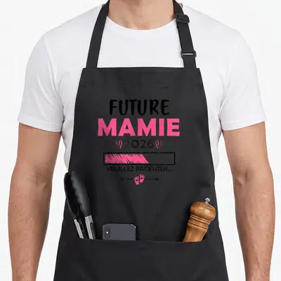Tablier de cuisine noir avec texte Future Mamie 2026 et icône de petites pattes roses