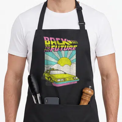 Tablier de cuisine noir avec une Delorean jaune, un soleil levant et le texte Back to the Future en couleurs vives.