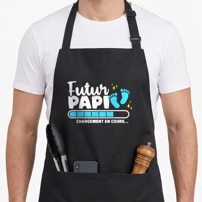Tablier de cuisine noir avec inscription Futur Papi chargement en cours et empreintes de pieds bleues.
