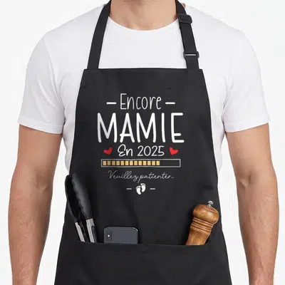 Tablier de cuisine noir avec le texte blanc Encore Mamie En 2025 et des petits pieds imprimés