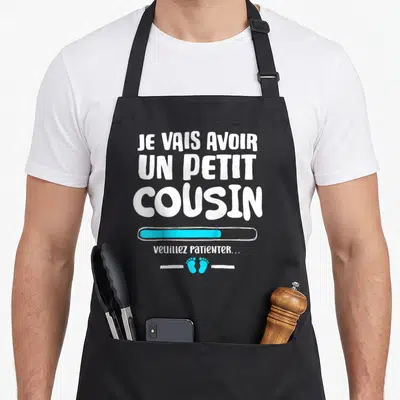 Tablier de cuisine noir avec inscription Je vais avoir un petit cousin et barres de chargement bleues.