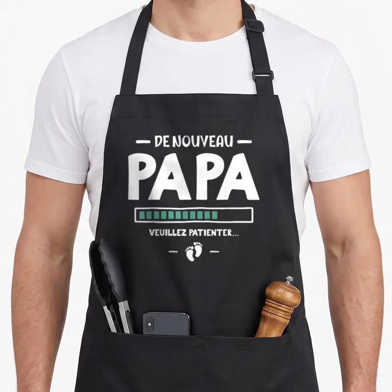 Tablier de cuisine noir avec texte blanc De nouveau Papa, barre de progression verte et empreintes de pieds.