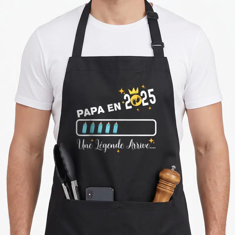 Tablier de cuisine noir avec inscription Papa en 2025 et cinq biberons bleus dans une barre de progression jaune et blanche.